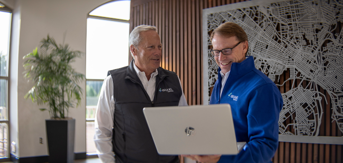 Two senior professionals smiling as they look at a laptop